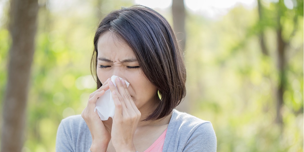 Een vrouw die haar neus snuit in het bos, omringd door bomen en natuur.